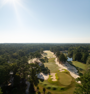 Aerial view of a sunny golf course with sand traps, green fairways, and surrounding trees.